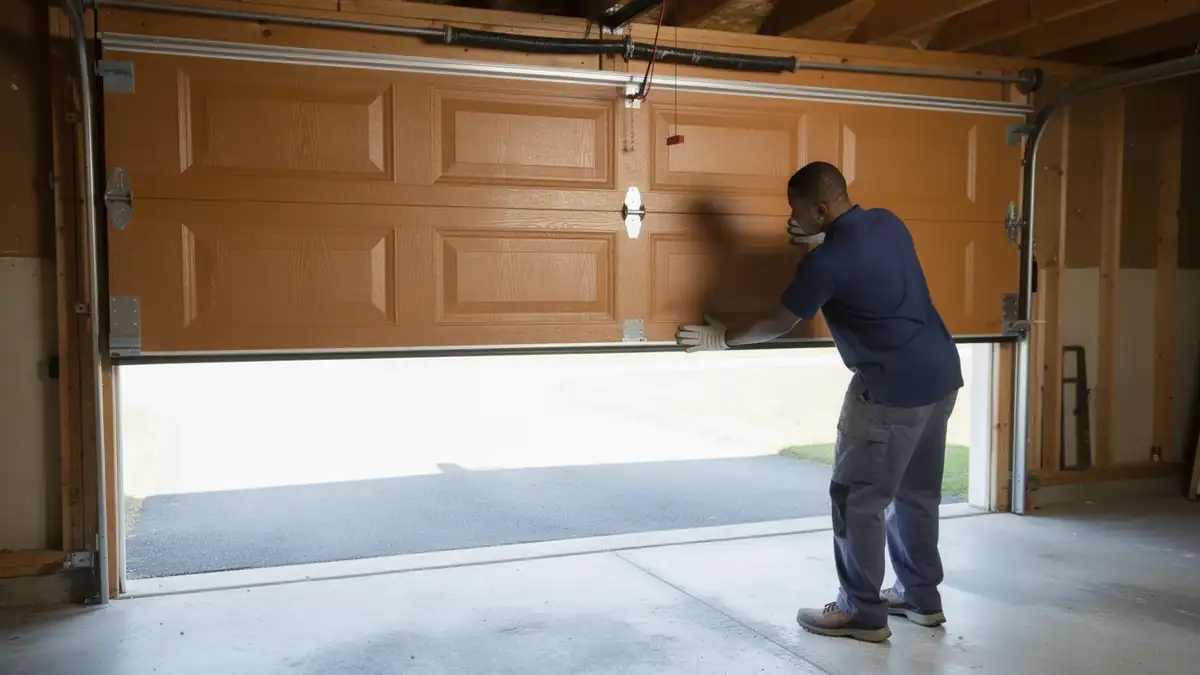 A technician in gloves is installing a brown garage door.